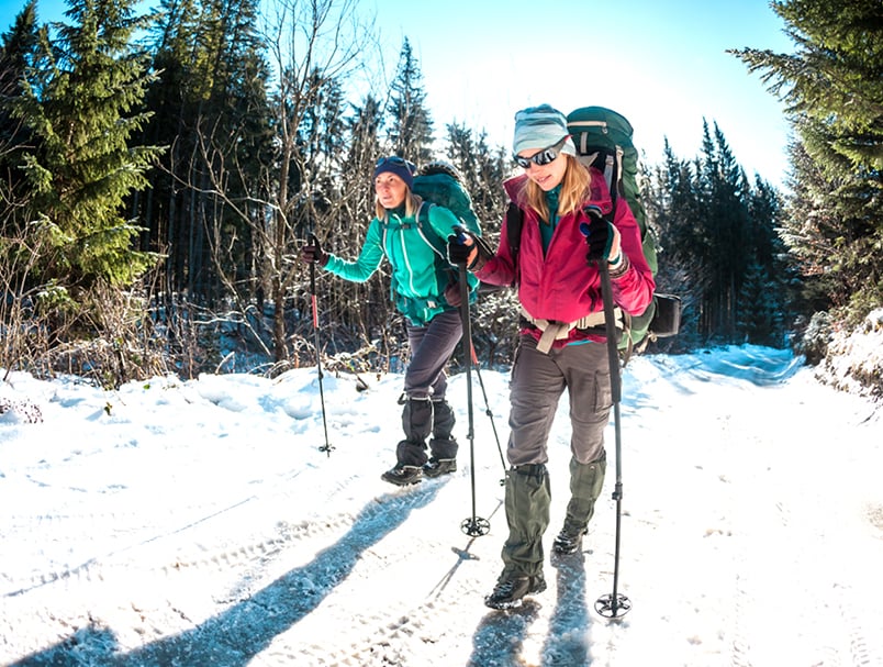 Two women hike along a snowy trail with ski polls