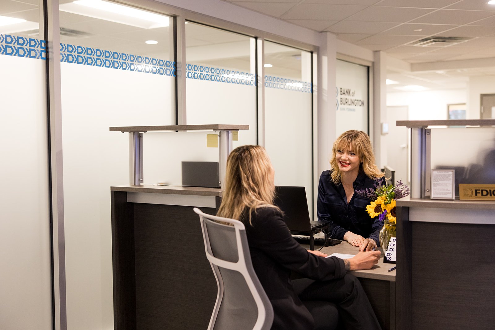 Smiling for the camera, the Bank of Burlington team sits at a round office table at their office